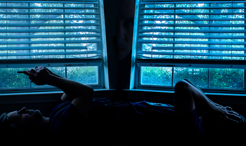 photograph of man in mirrored image looking at phone and hands on face.