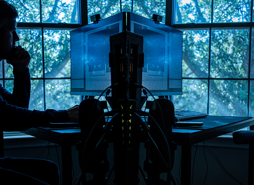 photograph of a man in a mirror image. one half of the photo he is at a computer desk in front of the window and in the other half it is the computer desk in front of the window but the man is gone.